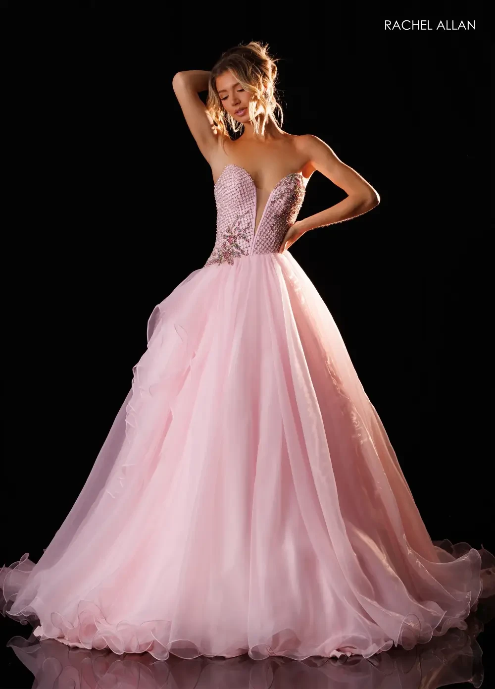 A woman wearing a strapless pink ball gown with a beaded bodice, posing gracefully against a black background.