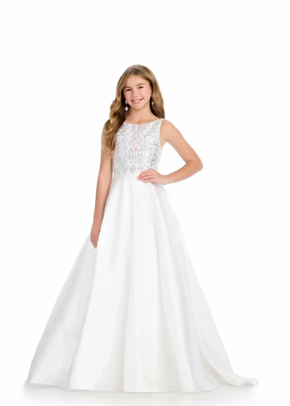 A young girl in a white formal dress with a decorative top and full skirt, standing with one hand on her hip.