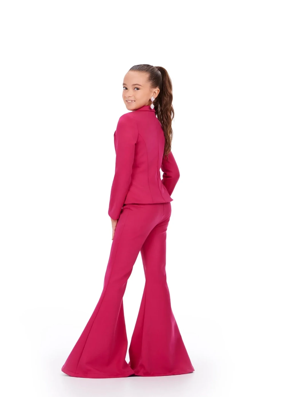 A young girl modeling the back of a vibrant pink pageant interview pantsuit with a tailored blazer and flared pants.