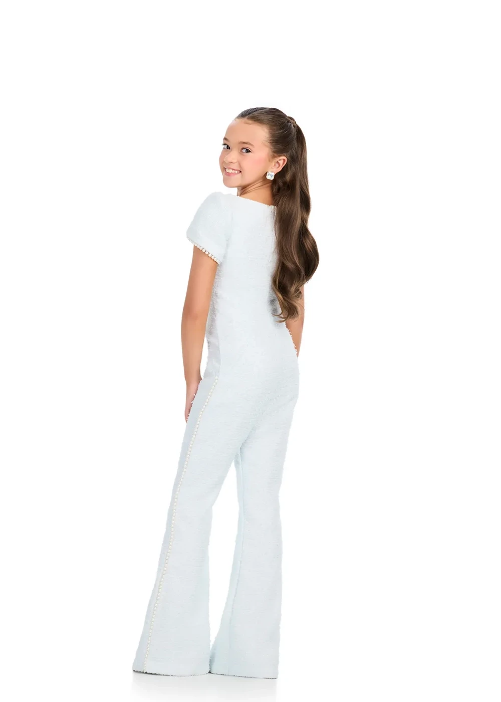 A young girl modeling the back of a light blue pageant interview jumpsuit with pearl-trimmed sides, short sleeves, and flared legs.